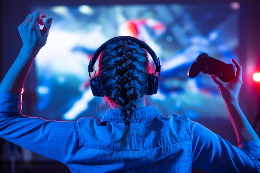 Young girl in headphones plays a video game on the TV in the eve
