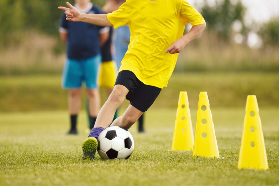 Football Drills: The Slalom Drill. Youth soccer practice drills. Young football players training on pitch. Soccer slalom cone drill. Boy in yellow soccer jersey shirt running with ball between cones